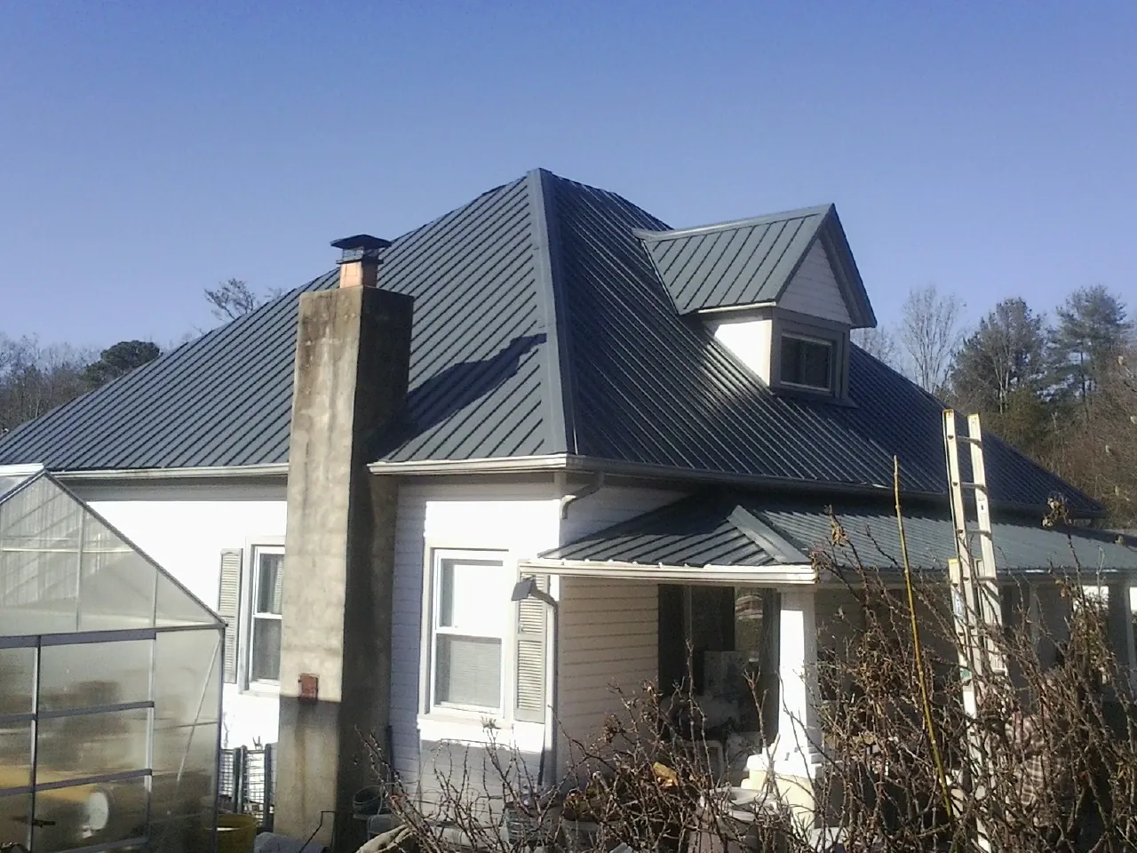 Dark blue standing seam metal roof on a white farmhouse with dormer — Slate & Tile Roof Repair by Roofing Brothers in Berkeley Springs