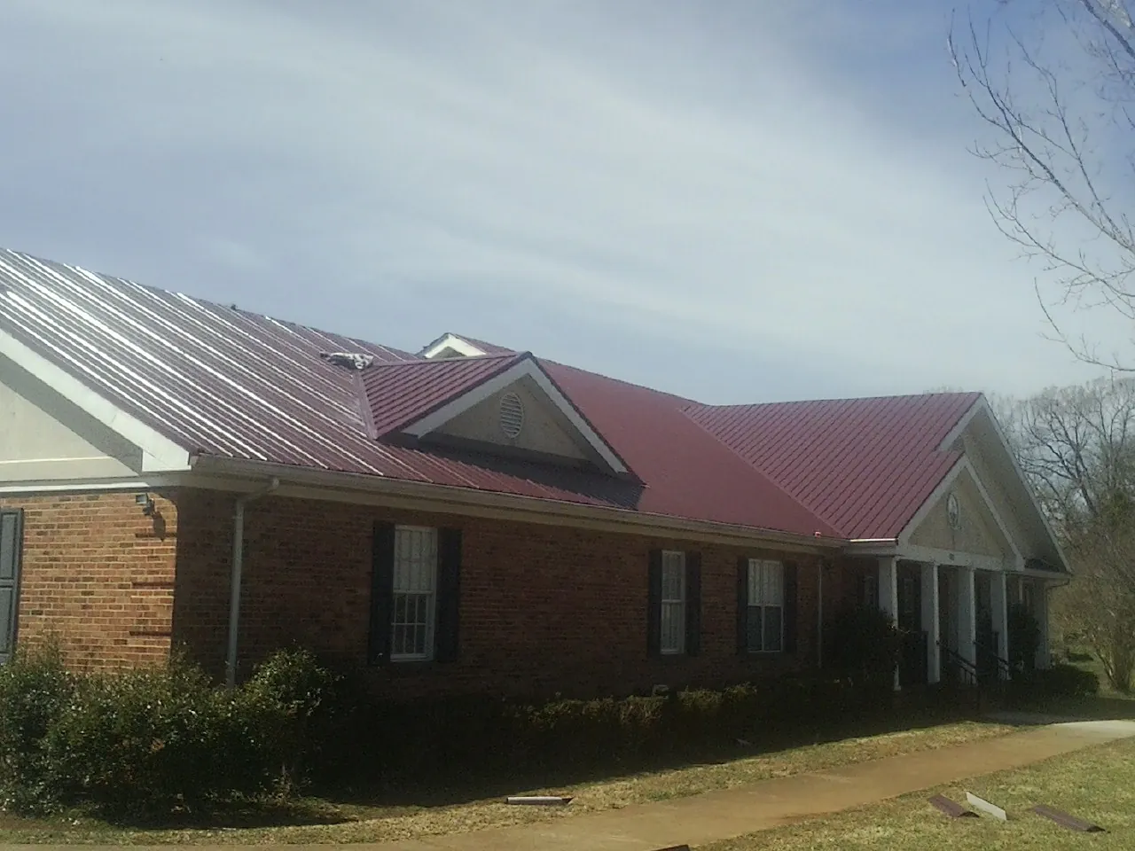 Red metal roof with gabled entries on a long brick building, from a Hail Damage Roof Repair job in Berkeley Springs
