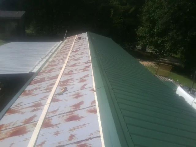Old rusted panels beside newly installed green metal roofing — Wind Damage Roof Repair by Roofing Brothers in Berkeley Springs