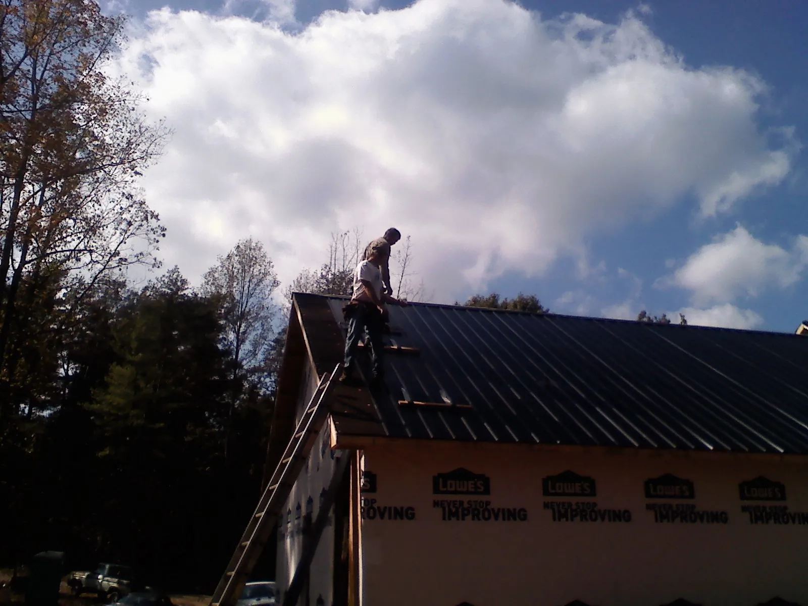 Roofer fastening dark metal panels high against a cloudy sky, from a Roof Inspection job in Berkeley Springs