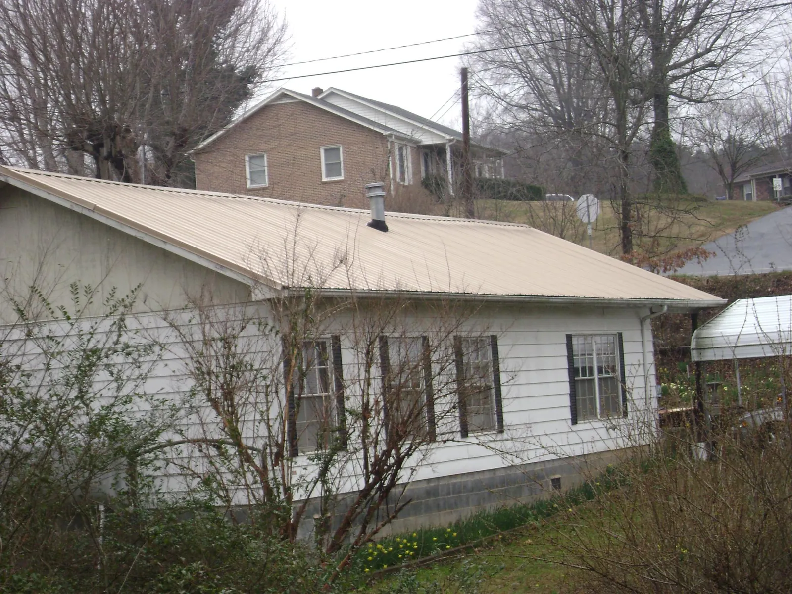 Tan metal roof on a white sided house set into a hillside — Commercial Roofing by Roofing Brothers in Berkeley Springs